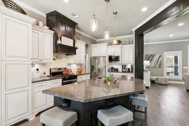 kitchen with a kitchen bar, dark stone counters, a center island with sink, appliances with stainless steel finishes, and dark hardwood / wood-style flooring