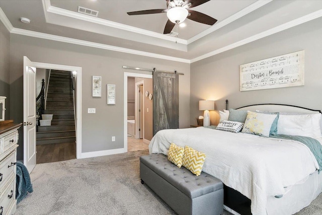 bedroom with ceiling fan, a barn door, ensuite bathroom, and a tray ceiling