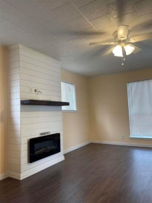 unfurnished living room featuring ceiling fan, a large fireplace, and dark wood-type flooring