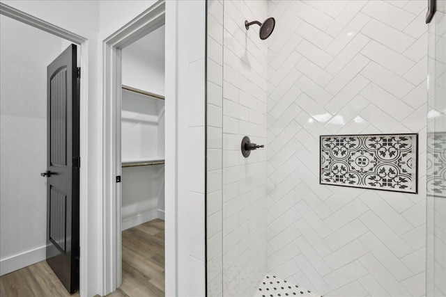 full bath with a spacious closet, tiled shower, baseboards, and wood finished floors