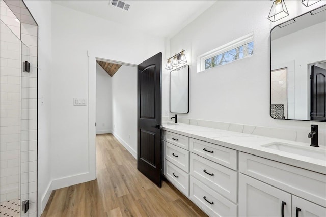 bathroom with visible vents, a sink, wood finished floors, a shower stall, and baseboards