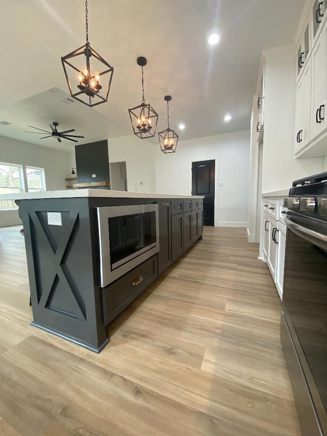 kitchen with a kitchen island, pendant lighting, light wood-type flooring, gas stove, and white cabinetry