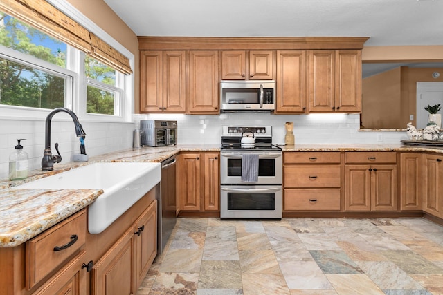 kitchen featuring sink, light stone counters, tasteful backsplash, and appliances with stainless steel finishes