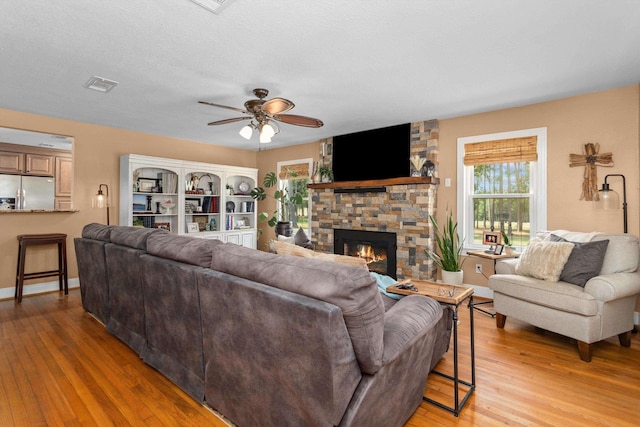 living room with light hardwood / wood-style floors, plenty of natural light, ceiling fan, and a stone fireplace