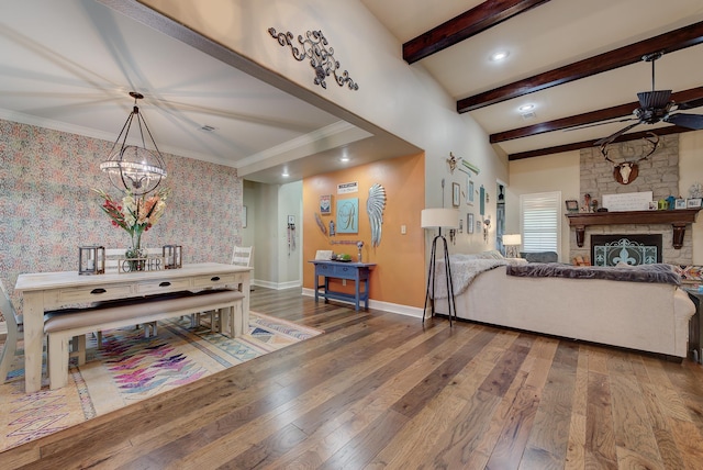 interior space featuring a stone fireplace, beamed ceiling, wood-type flooring, and ceiling fan with notable chandelier