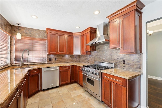 kitchen with pendant lighting, wall chimney range hood, sink, appliances with stainless steel finishes, and light stone counters