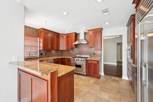 kitchen with sink, high end appliances, kitchen peninsula, light stone countertops, and wall chimney range hood