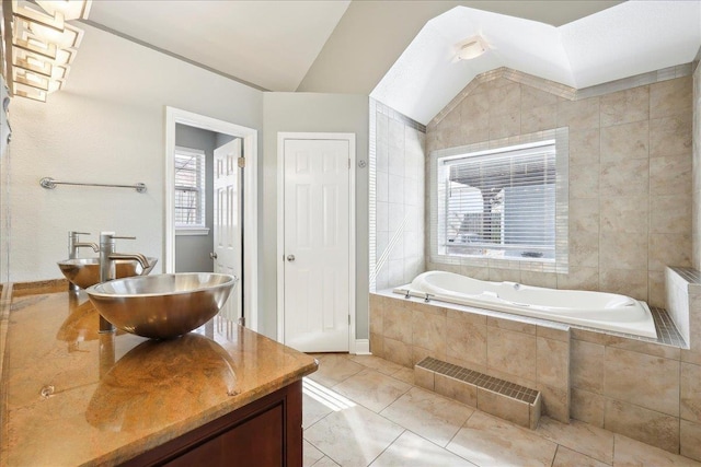 bathroom with a relaxing tiled tub, vanity, vaulted ceiling, and tile patterned floors