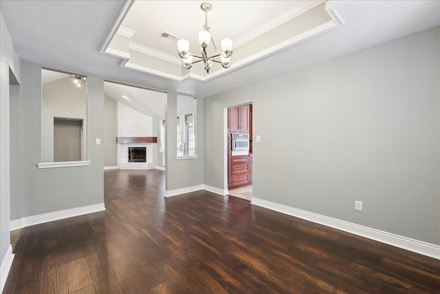 unfurnished living room with crown molding, a brick fireplace, a tray ceiling, dark hardwood / wood-style flooring, and a notable chandelier