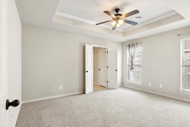 unfurnished room featuring a raised ceiling, ceiling fan, light carpet, and ornamental molding