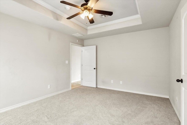 empty room with ceiling fan, a raised ceiling, ornamental molding, and light carpet