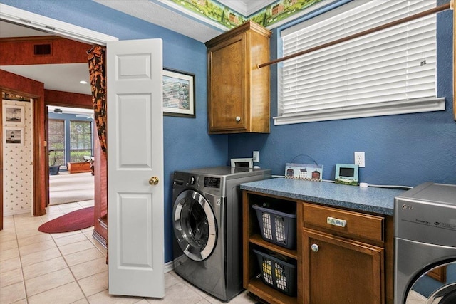 laundry room featuring washing machine and clothes dryer, light tile patterned flooring, and cabinets