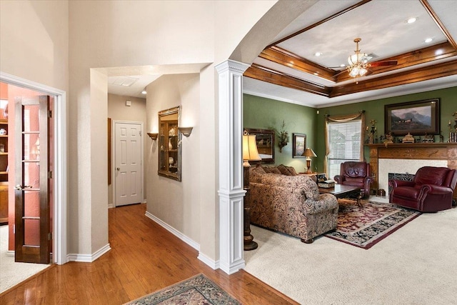 living room featuring decorative columns, ornamental molding, a tray ceiling, ceiling fan, and hardwood / wood-style floors