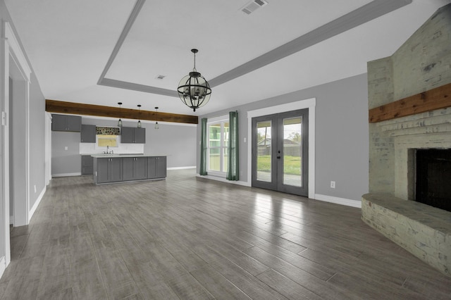 unfurnished living room featuring a stone fireplace, french doors, dark wood-type flooring, and a notable chandelier