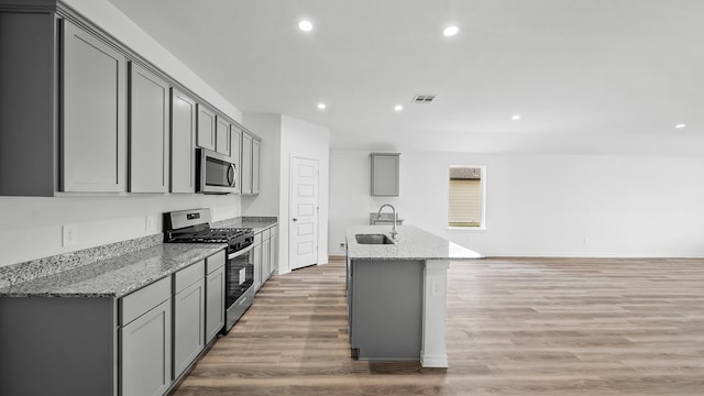 kitchen featuring appliances with stainless steel finishes, light wood-type flooring, light stone counters, gray cabinetry, and sink