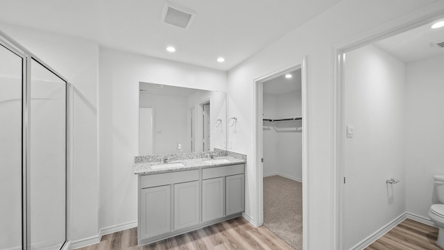 bathroom featuring hardwood / wood-style flooring, vanity, a shower with shower door, and toilet