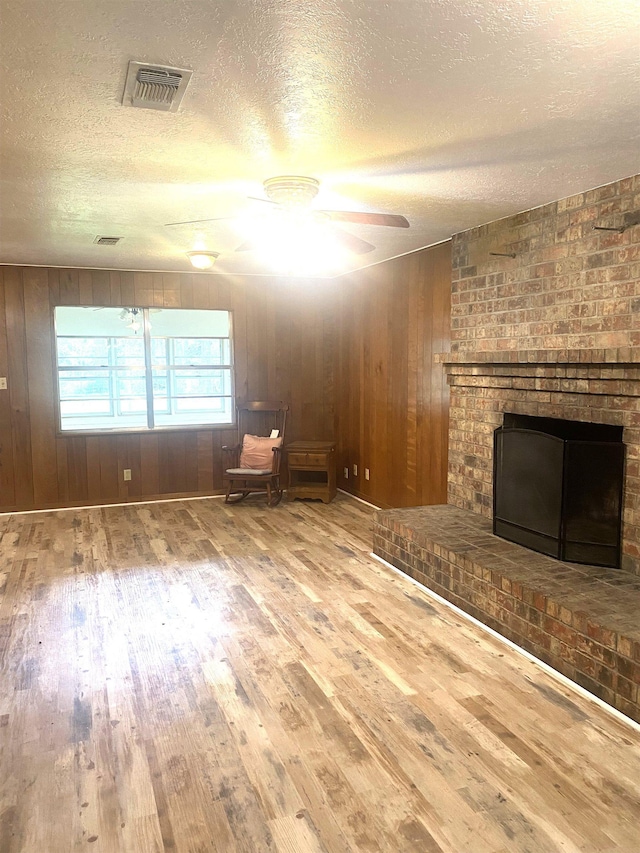 unfurnished living room with ceiling fan, visible vents, a brick fireplace, and wood finished floors