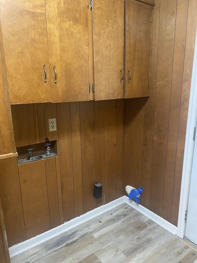 clothes washing area featuring wood walls, light wood-style floors, and baseboards