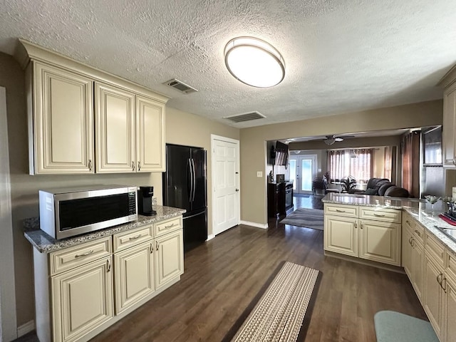 kitchen featuring visible vents, cream cabinetry, freestanding refrigerator, dark wood-style floors, and stainless steel microwave