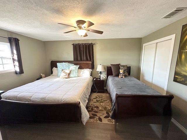 bedroom with a textured ceiling, wood finished floors, visible vents, a ceiling fan, and a closet