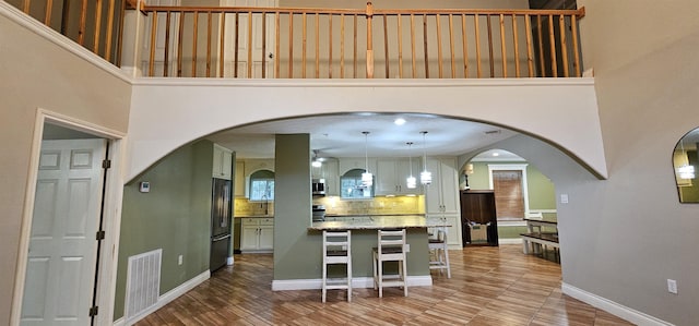 kitchen featuring appliances with stainless steel finishes, backsplash, a kitchen breakfast bar, pendant lighting, and a high ceiling