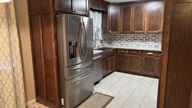 kitchen featuring light stone counters, dark brown cabinets, stainless steel appliances, sink, and light tile patterned floors