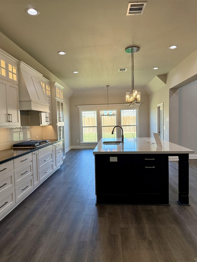kitchen featuring visible vents, a sink, premium range hood, dark wood-style flooring, and a kitchen island with sink
