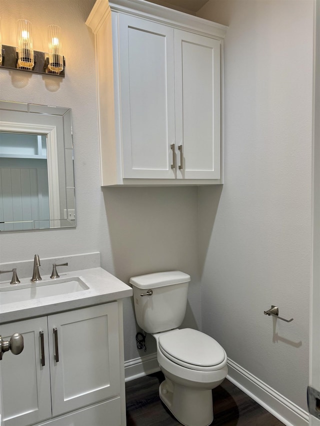 bathroom with toilet, vanity, baseboards, and wood finished floors