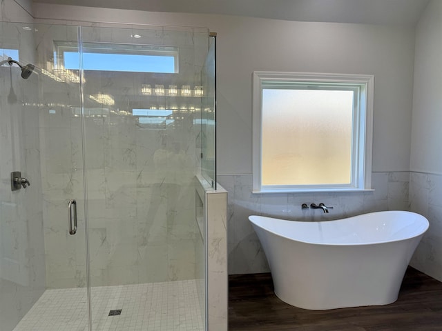 full bath featuring a marble finish shower, a soaking tub, wainscoting, and wood finished floors