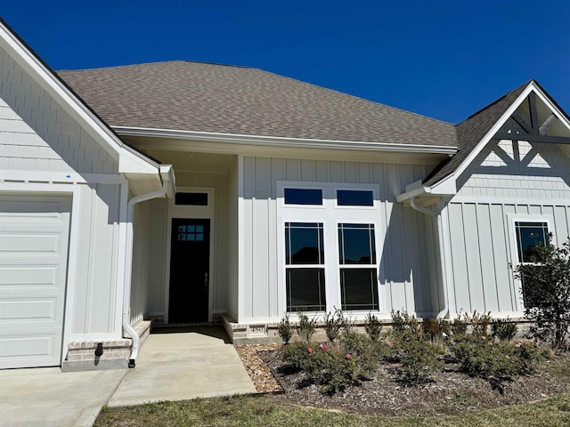 doorway to property featuring an attached garage, board and batten siding, and roof with shingles