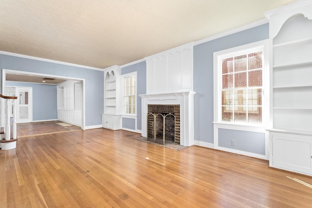 unfurnished living room featuring stairway, built in features, light wood-style floors, crown molding, and a brick fireplace