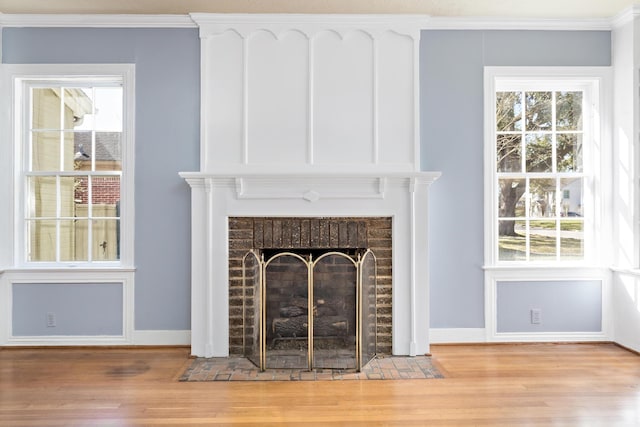 interior details featuring baseboards, a brick fireplace, wood finished floors, and crown molding