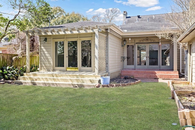 back of property featuring fence, entry steps, roof with shingles, a lawn, and french doors