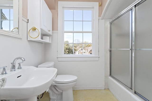 full bath featuring toilet, shower / bath combination with glass door, and a sink