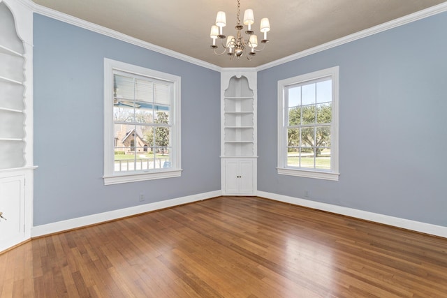 empty room with crown molding, baseboards, built in features, an inviting chandelier, and hardwood / wood-style flooring