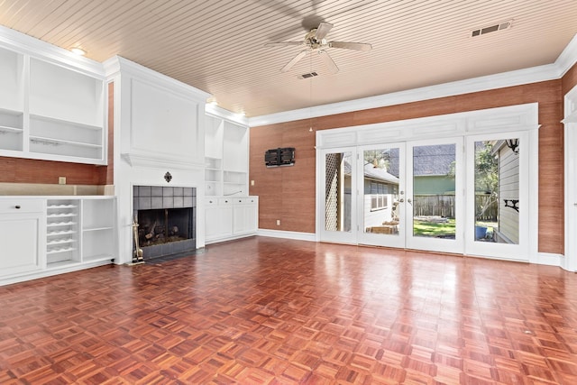 unfurnished living room with built in shelves, a ceiling fan, visible vents, wood walls, and a tiled fireplace