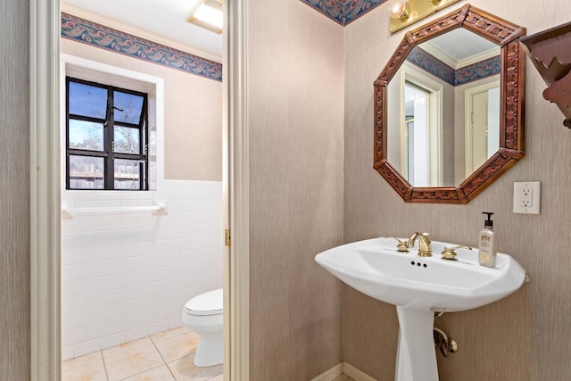 half bath featuring wallpapered walls, tile patterned flooring, wainscoting, tile walls, and toilet