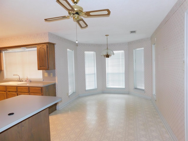 6340 Capitol St, Groves, TX 77619 - kitchen featuring light countertops, light flooring, wallpapered walls, brown cabinets, and decorative light fixtures
