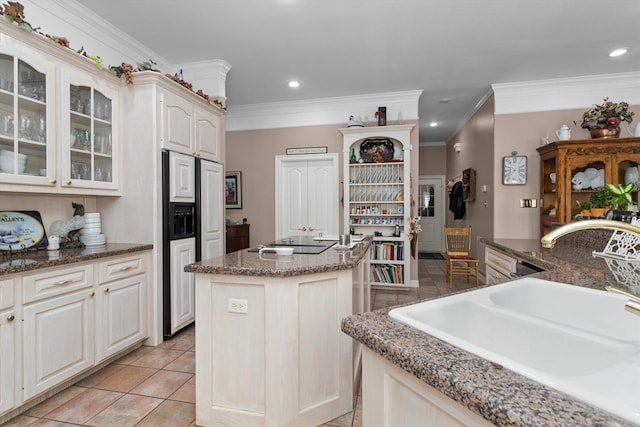 kitchen with dark stone counters, a kitchen island, crown molding, and sink