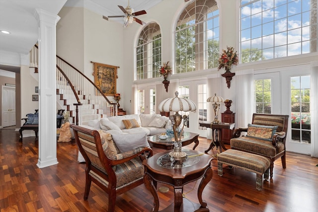 living room with a high ceiling, decorative columns, ceiling fan, and dark wood-type flooring