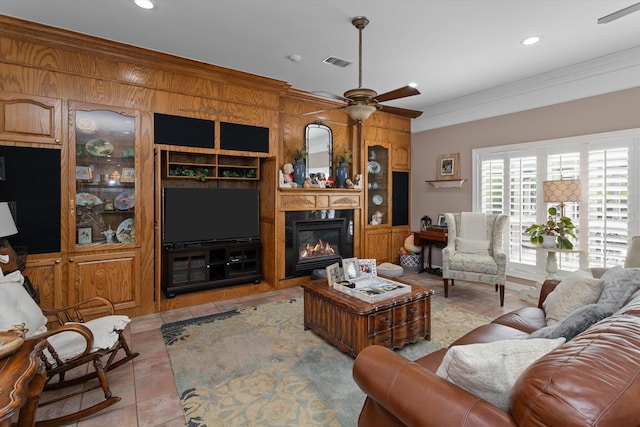 living room featuring a fireplace, ceiling fan, built in features, and crown molding