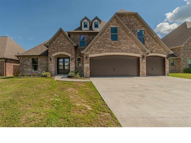 french country home with an attached garage, brick siding, driveway, and a front yard