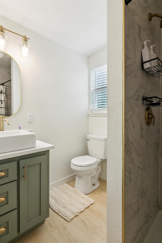 full bathroom with baseboards, tiled shower, toilet, wood finished floors, and vanity