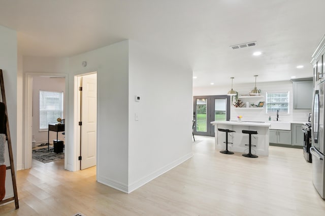 kitchen featuring light wood-style flooring, a sink, light countertops, open shelves, and a kitchen bar