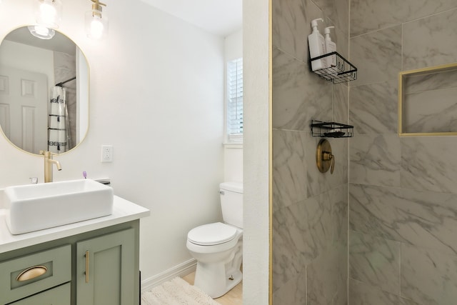 bathroom with vanity, a tile shower, toilet, and baseboards