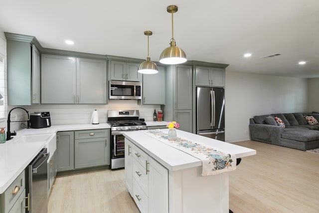 kitchen with light wood finished floors, stainless steel appliances, light countertops, open floor plan, and a sink