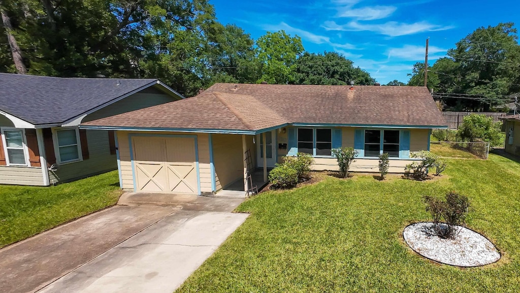 ranch-style home with a front yard, roof with shingles, a garage, and driveway