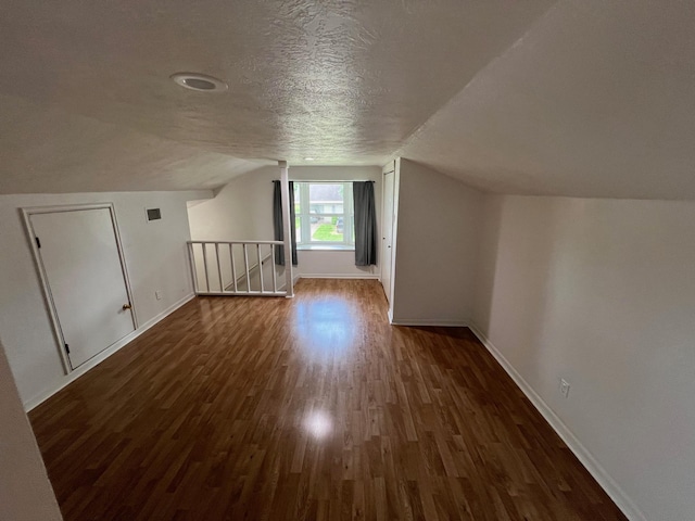 additional living space featuring a textured ceiling, dark wood-style flooring, vaulted ceiling, and baseboards