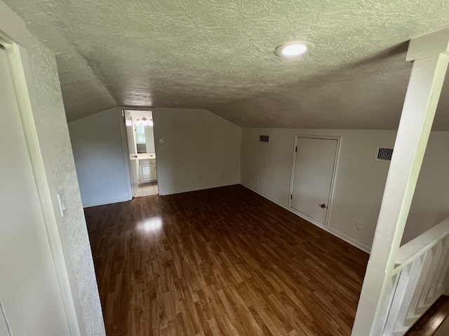 additional living space featuring wood finished floors, vaulted ceiling, baseboards, visible vents, and a textured ceiling