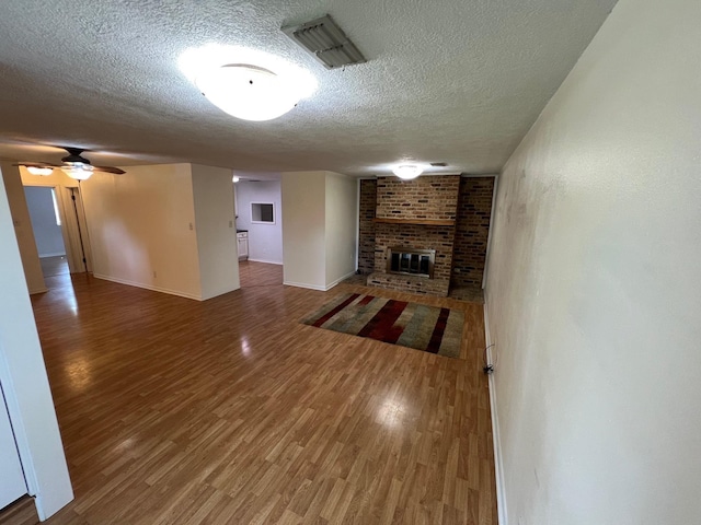 unfurnished living room featuring a fireplace, visible vents, baseboards, a textured ceiling, and wood finished floors
